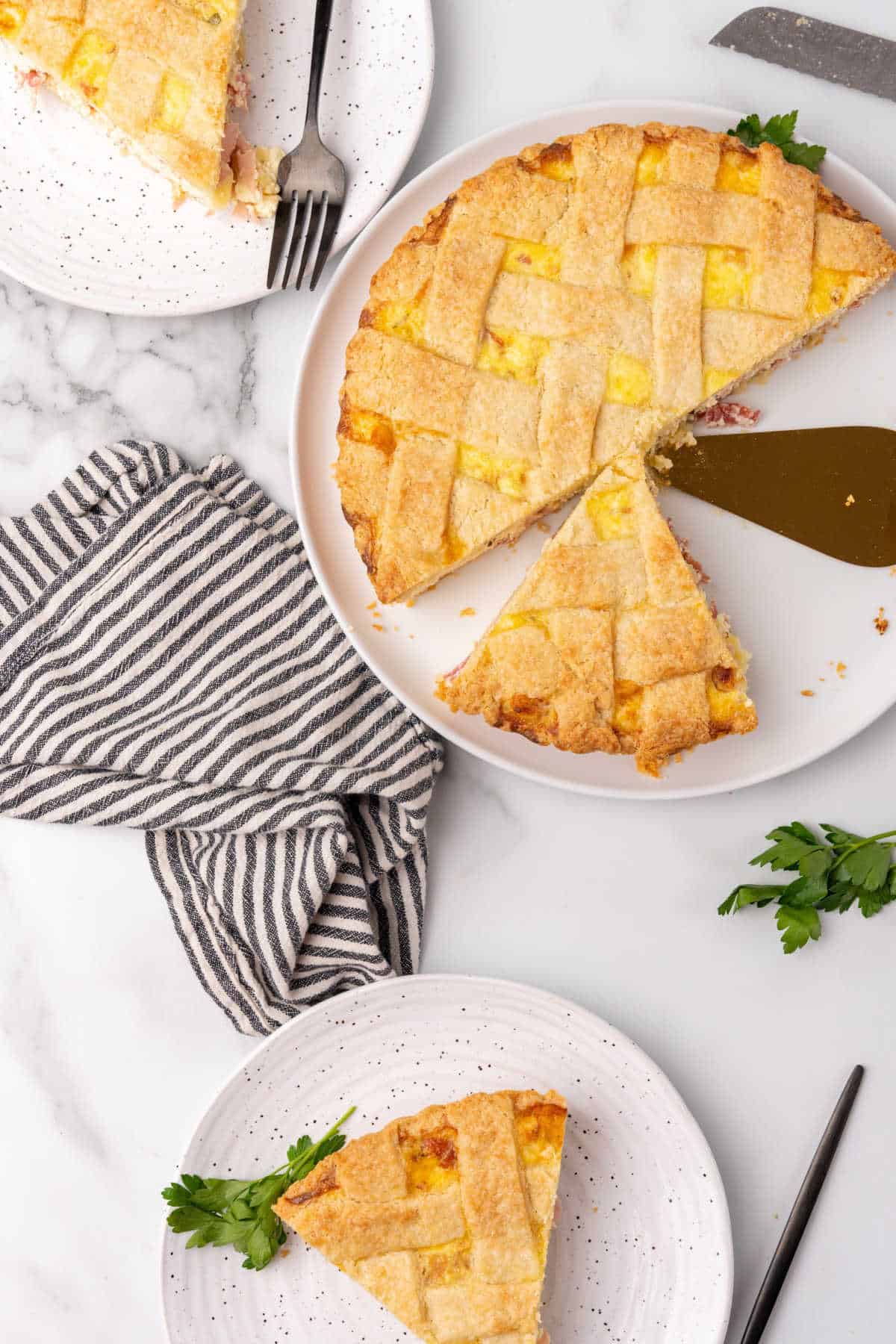 White marble with striped cloth and white plates with slices and pieces of lattice ricotta pie. 