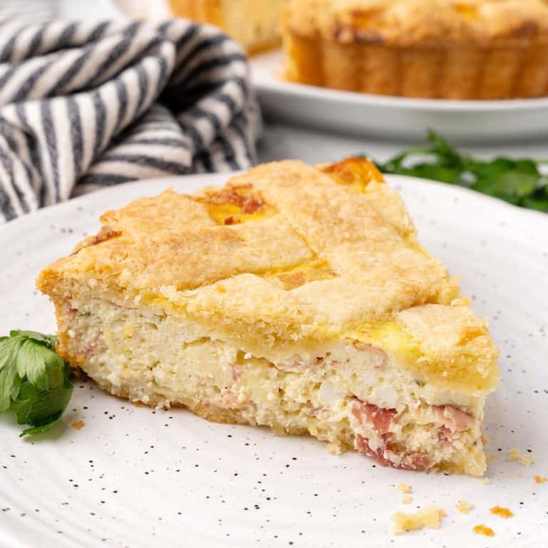 Single slice of savory ricotta lattice pie on a white plate. Striped cloth and rest of pie in the background.