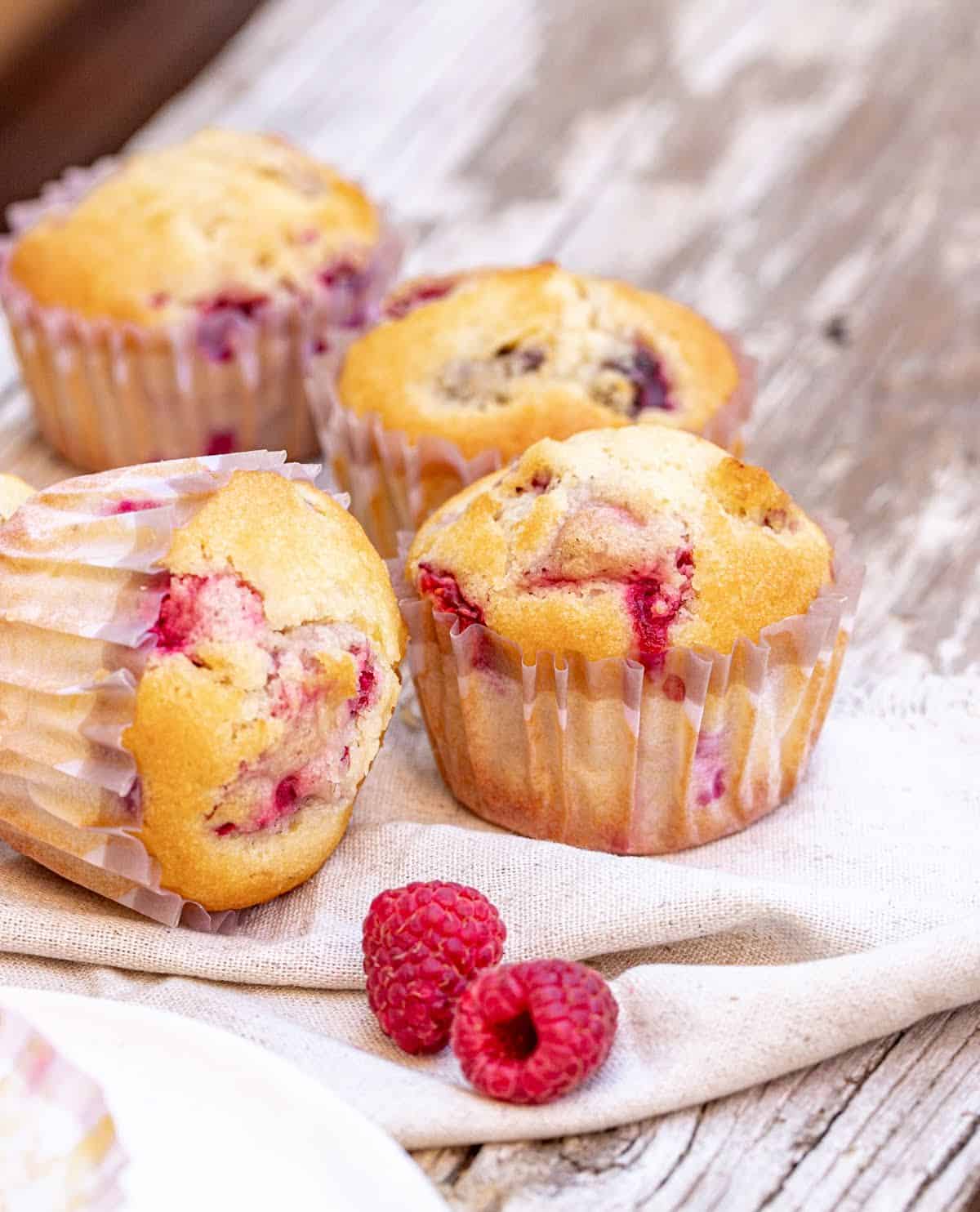 Grey wooden surface with raspberry muffins in paper cups.