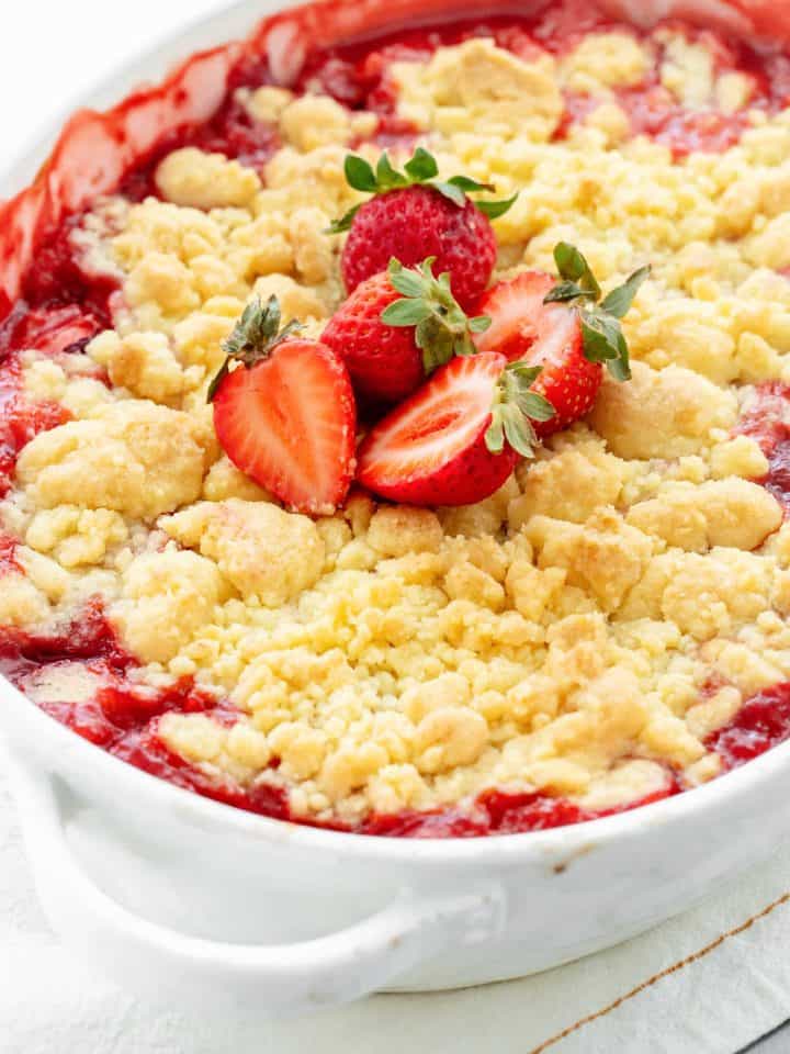 Baked strawberry dump cake in oval white dish with fresh strawberries on top; partial image.