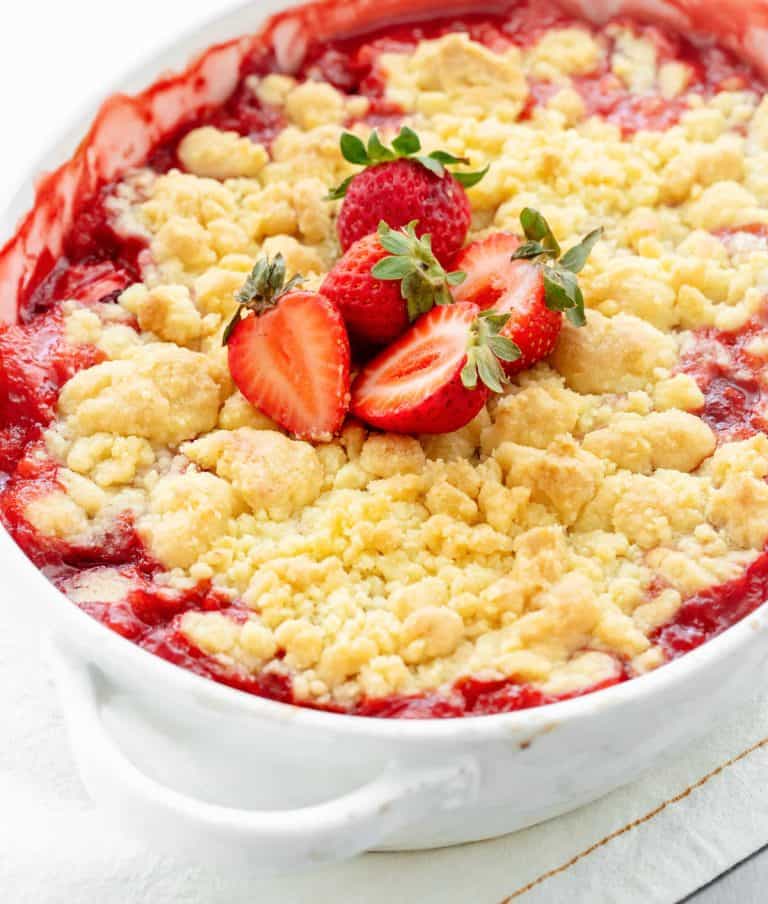 Baked strawberry dump cake in oval white dish with fresh strawberries on top; partial image.