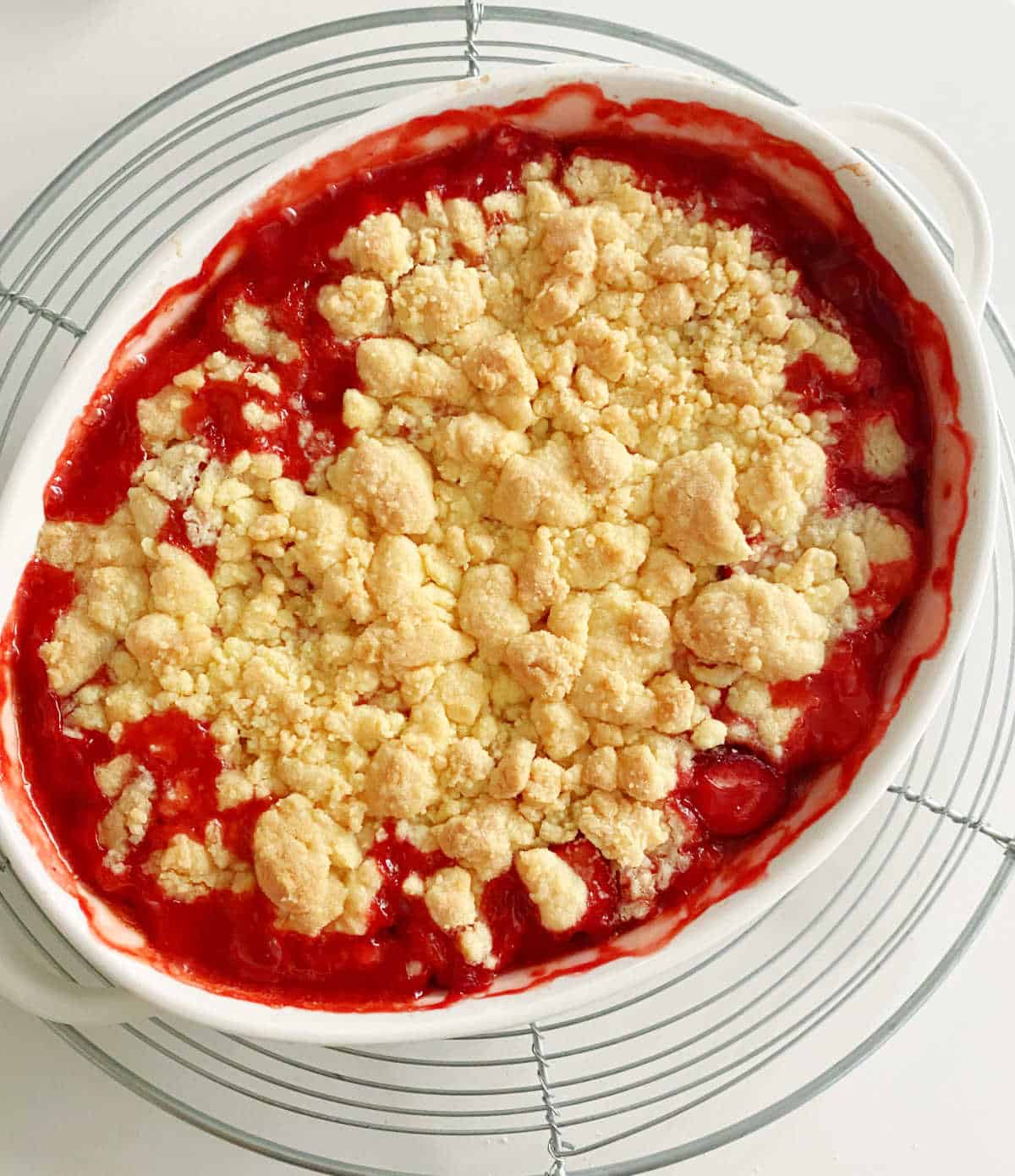 Just baked strawberry cobbler on a metal wire rack on a white surface. Top view.