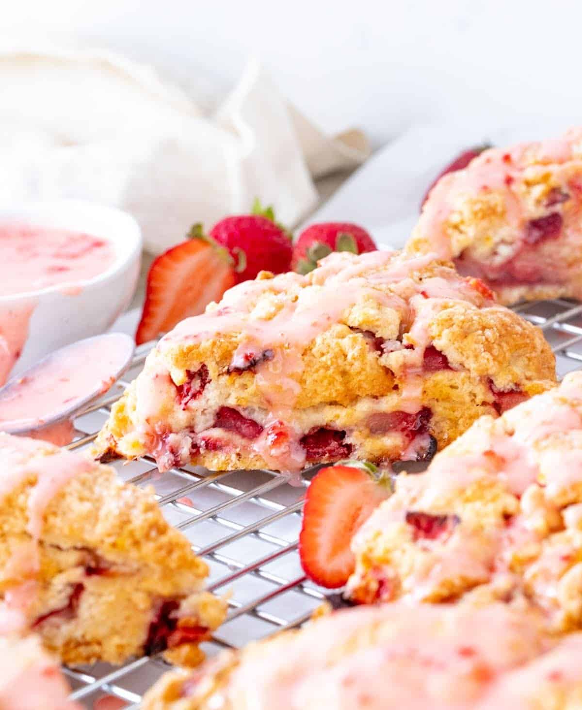 Close up of several glazed strawberry scones on wire rack, white background.