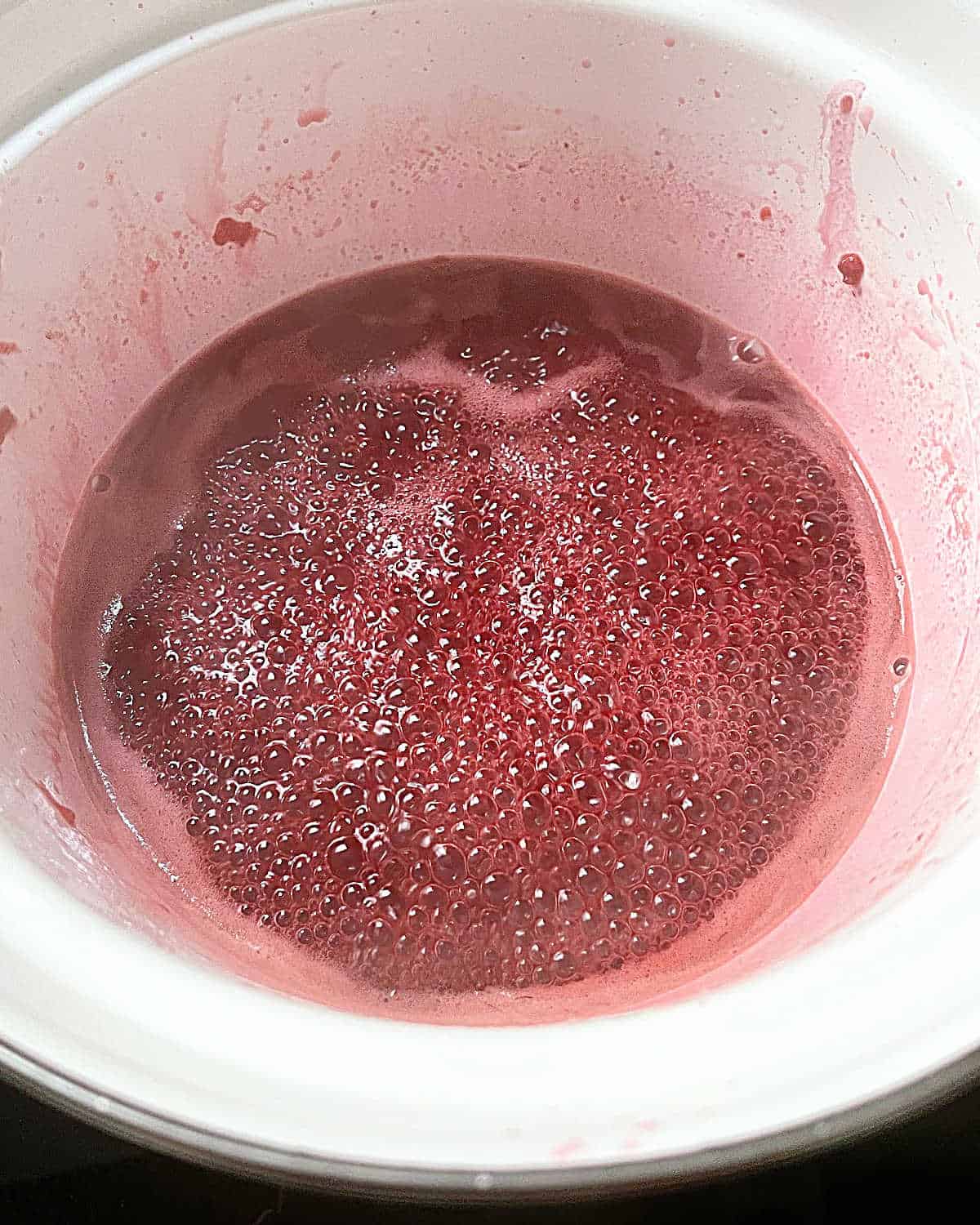 Reducing berry syrup in a white saucepan.