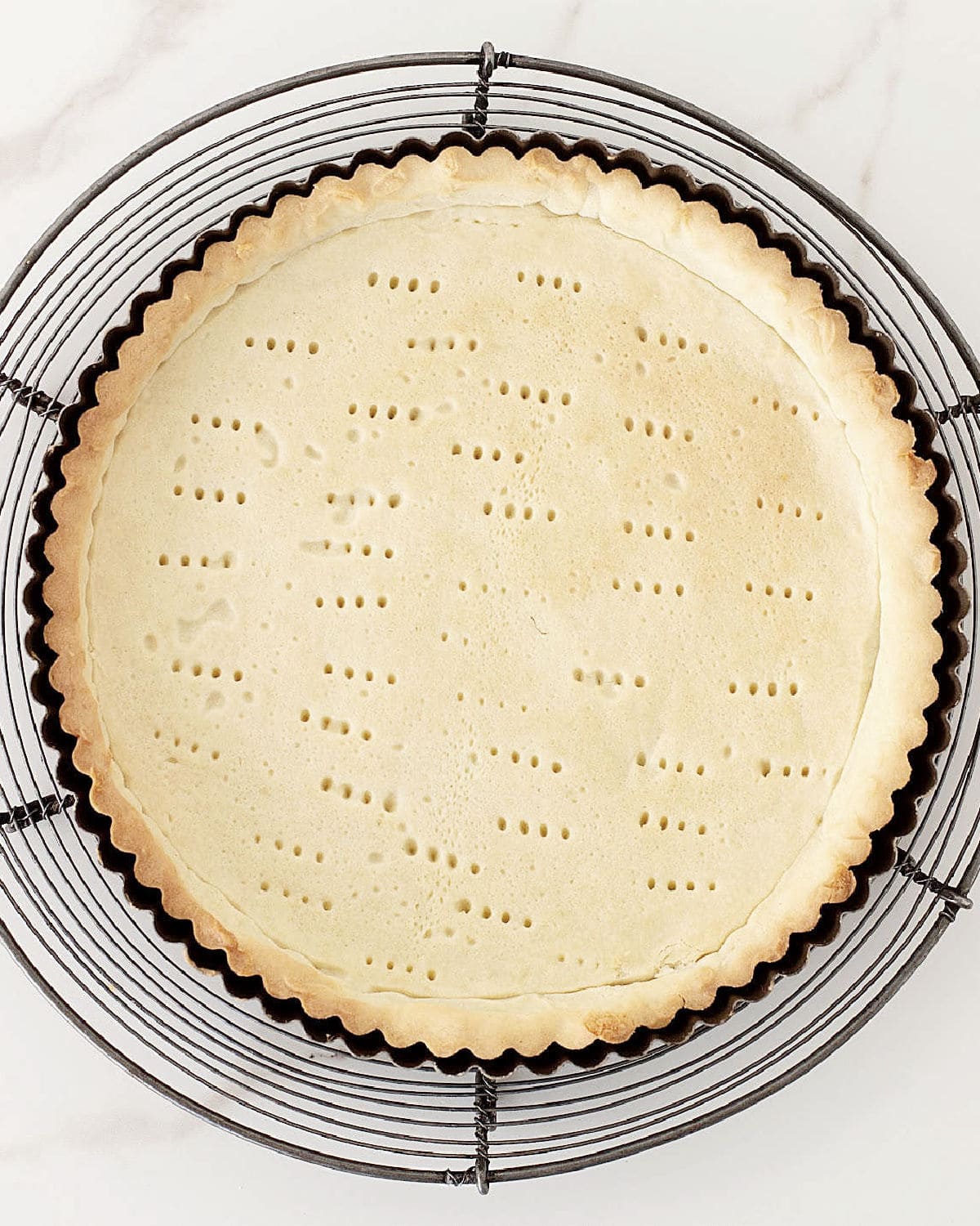 Blind baked tart crust in round metal pan on a wire rack.