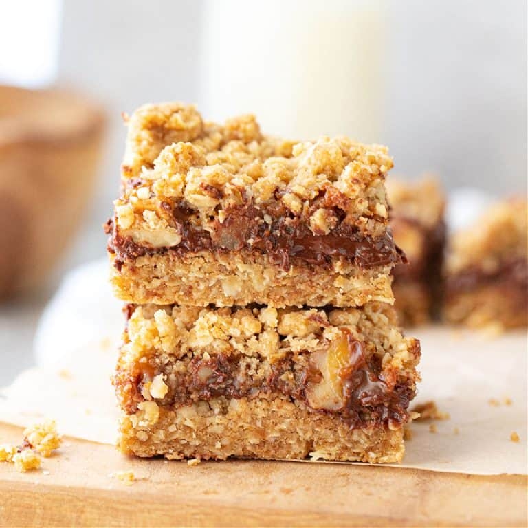 Stacked oatmeal chocolate bars on white paper on wooden board, grey white background.