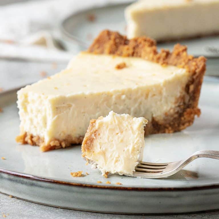 A slice of cheesecake pie on grey plate, bite of cheesecake on a silver fork.