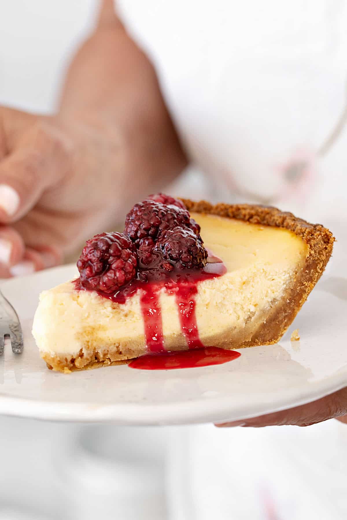 Blackberry sauce topped slice of cheesecake pie on a white plate.