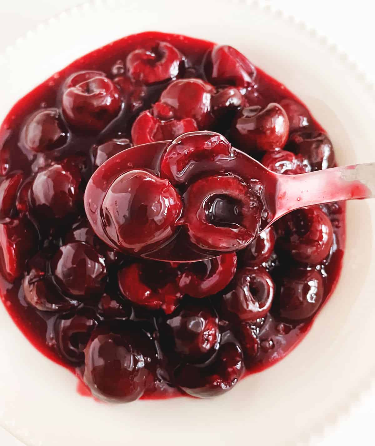 Spoon with cherry sauce over white bowl of more sauce.