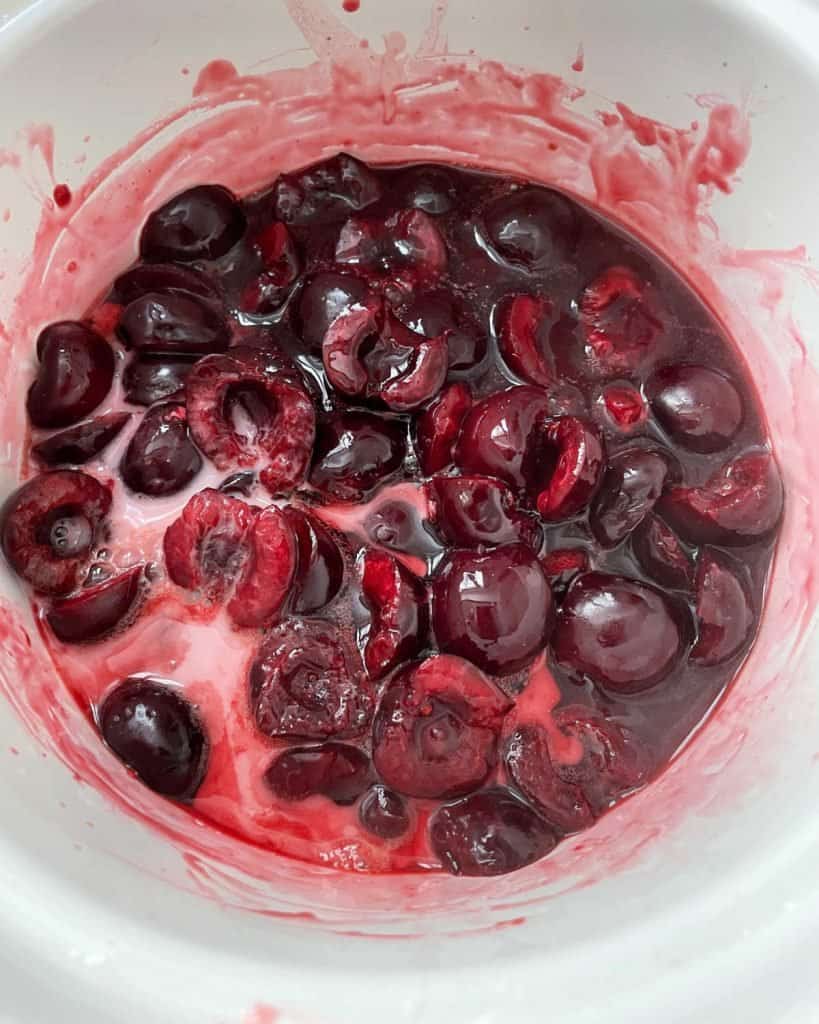 Top view of cherry sauce boiling in white saucepan.