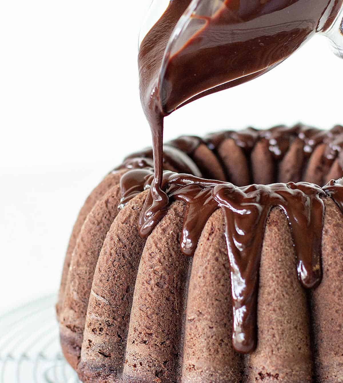 Ganache being poured over chocolate bundt cake on wire rack, white background.