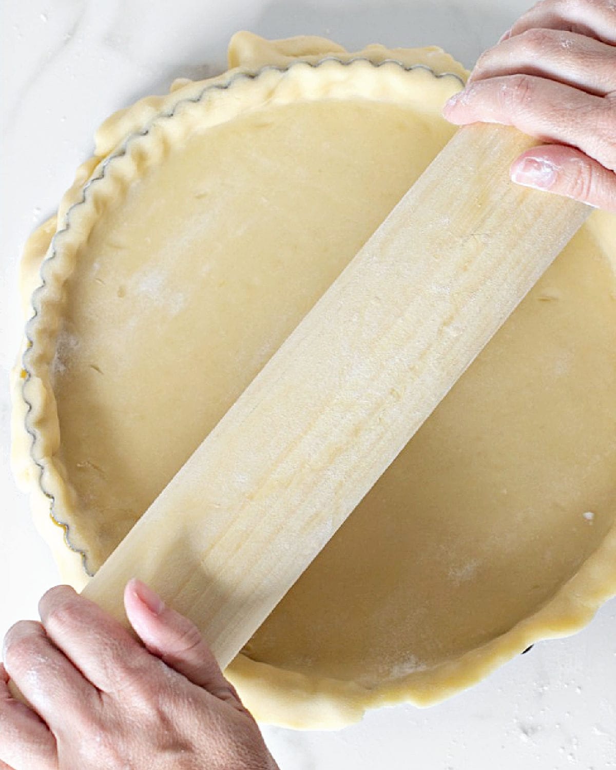 Rolling wooden pin over pie crust in a round pan. White marble surface.