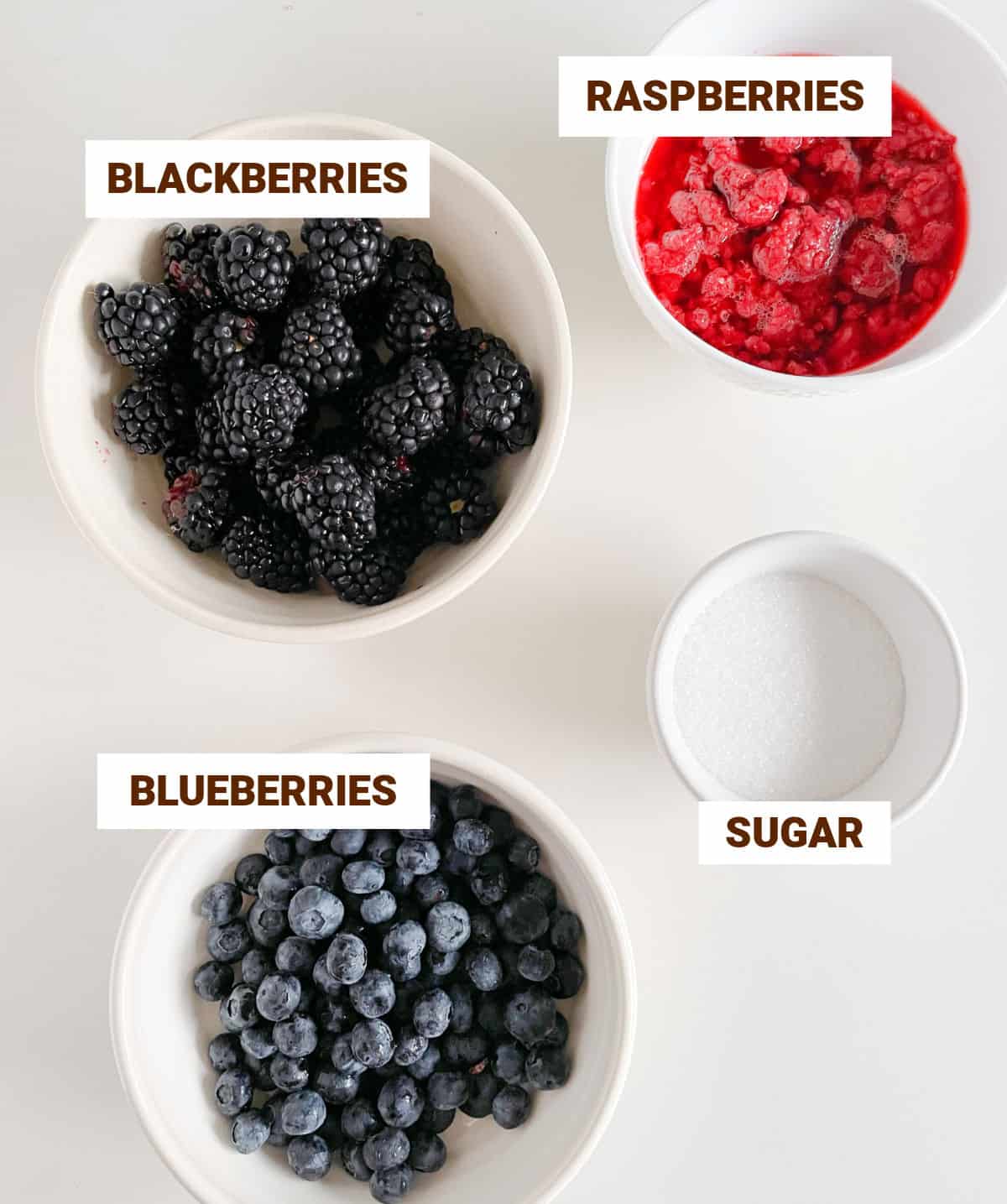 White surface with white bowls containing different berries and sugar. Image with text overlay.