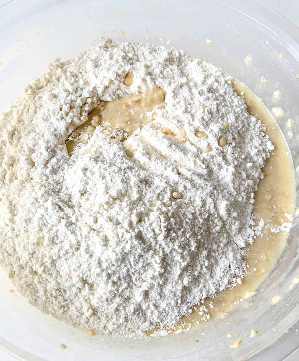 Flour added to oatmeal muffin batter in a glass bowl.