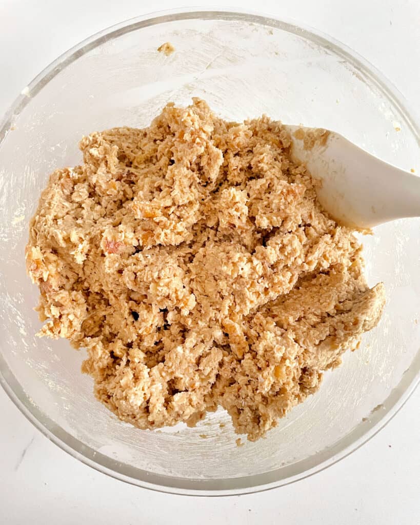 Oatmeal walnut cookie dough with a white spatula in a glass bowl.