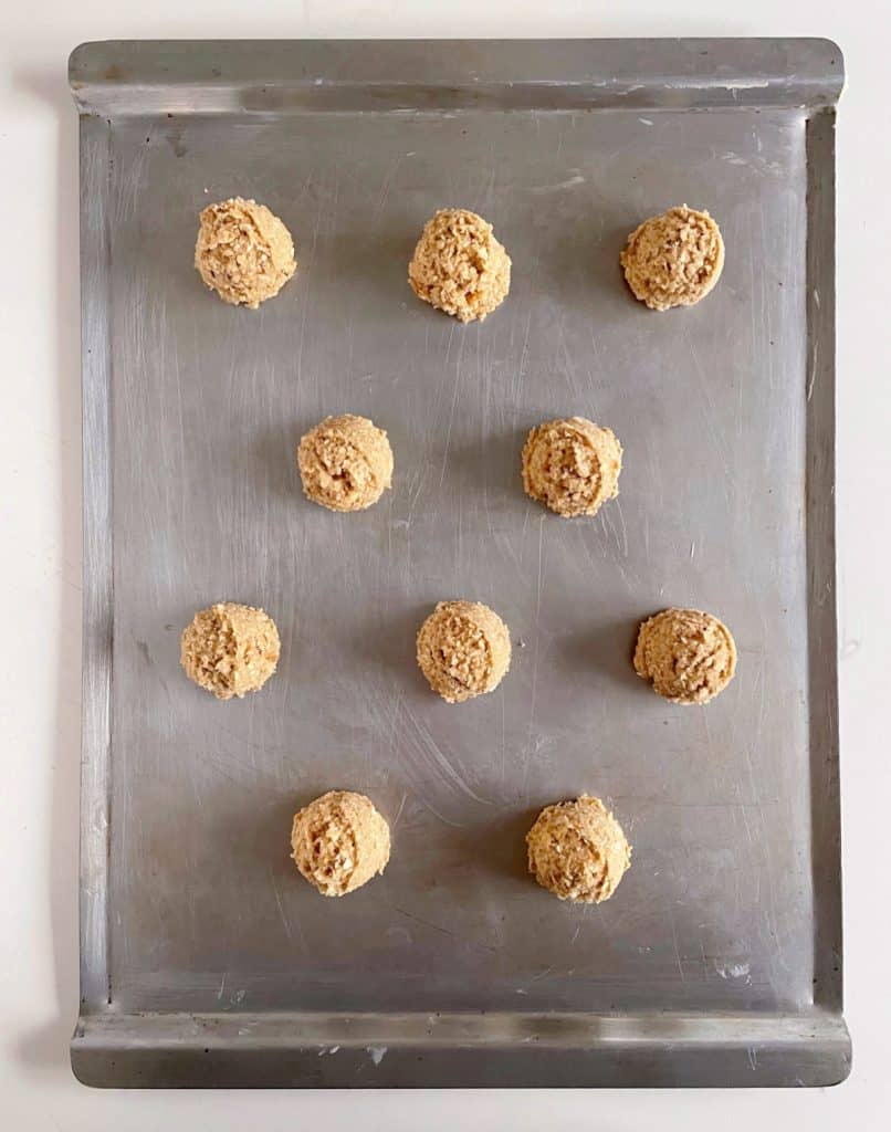 Overview of metal sheet pan with unbaked oatmeal cookies with walnuts.