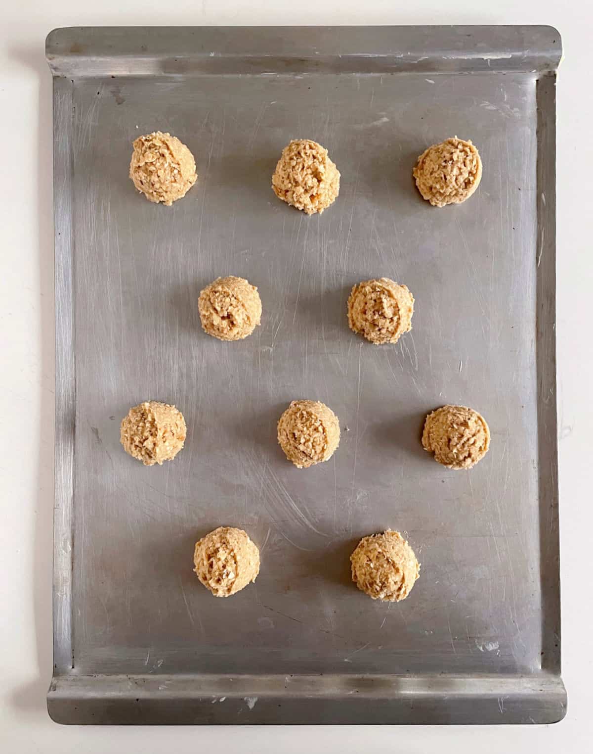 Overview of metal sheet pan with unbaked oatmeal cookies.