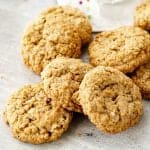 Several oatmeal cookies heaped together on grey surface, color dotted white linen in background.