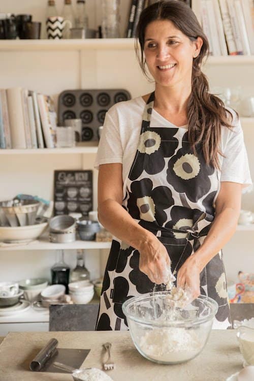 Dark hair person with apron working flour in glass bowl.