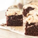 Beige parchment paper with squares of cinnamon frosted chocolate cake.