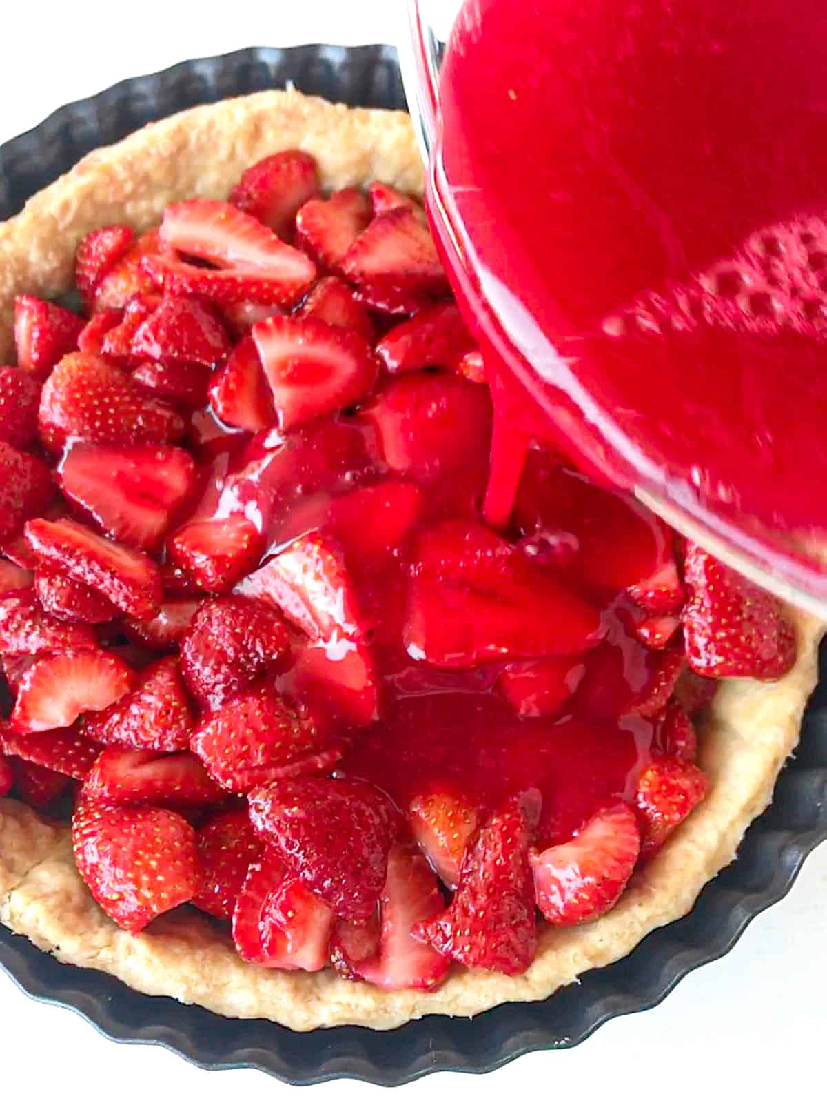 Pouring strawberry gelatin syrup over strawberry filling in a pie shell. White background.