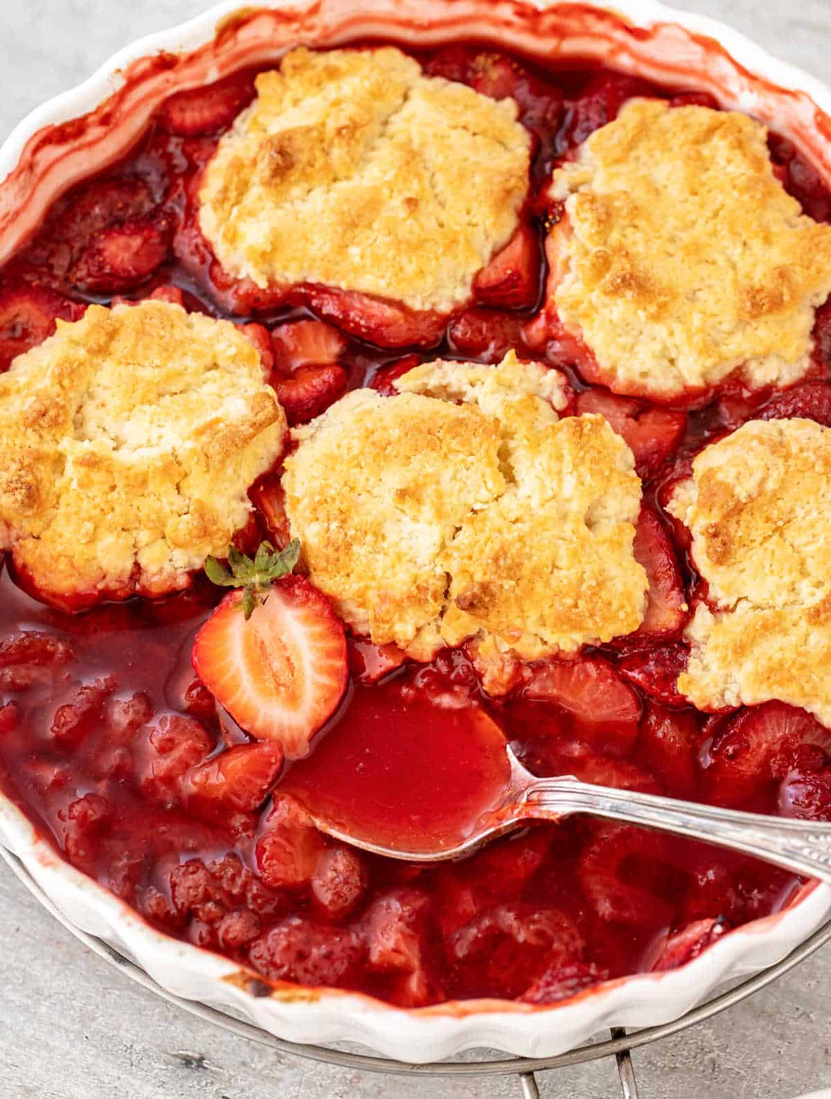 Partial view of round white dish with baked strawberry cobbler on grey surface.