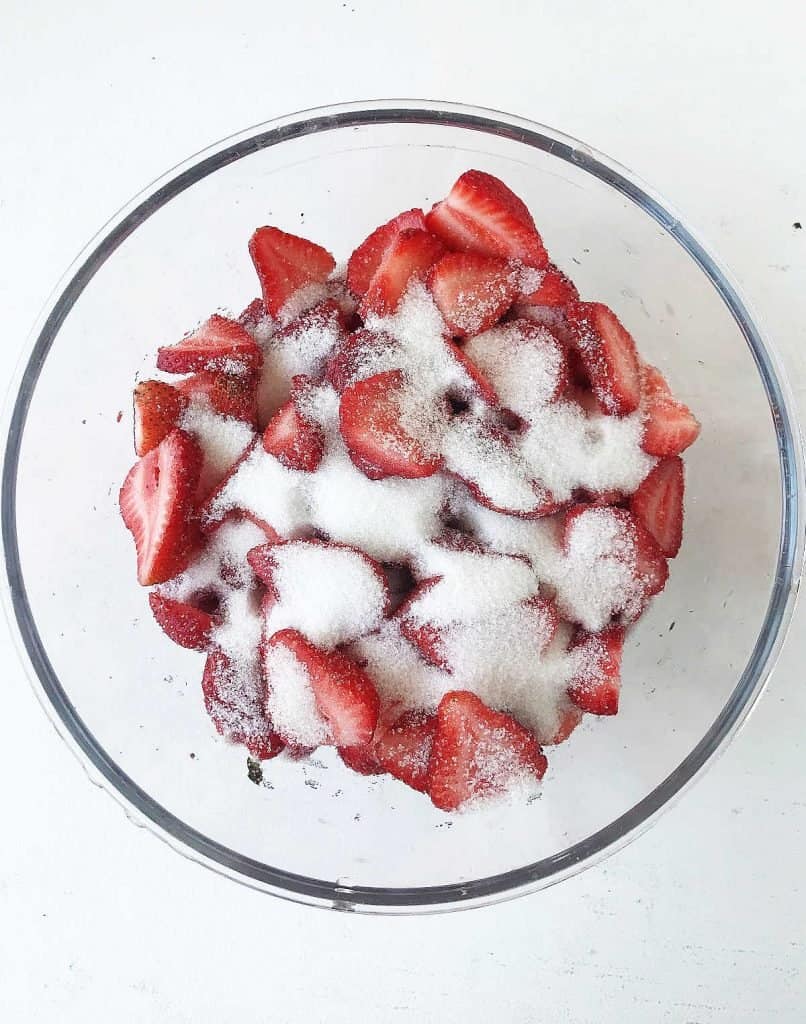 Glass bowl with strawberry pieces and sugar. White background.