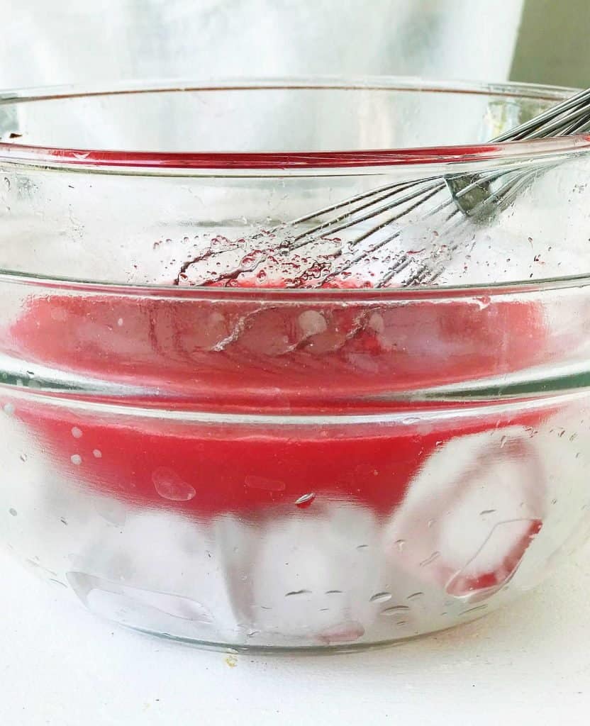 Ice glass bowl with another bowl on top with strawberry juice and whisk.