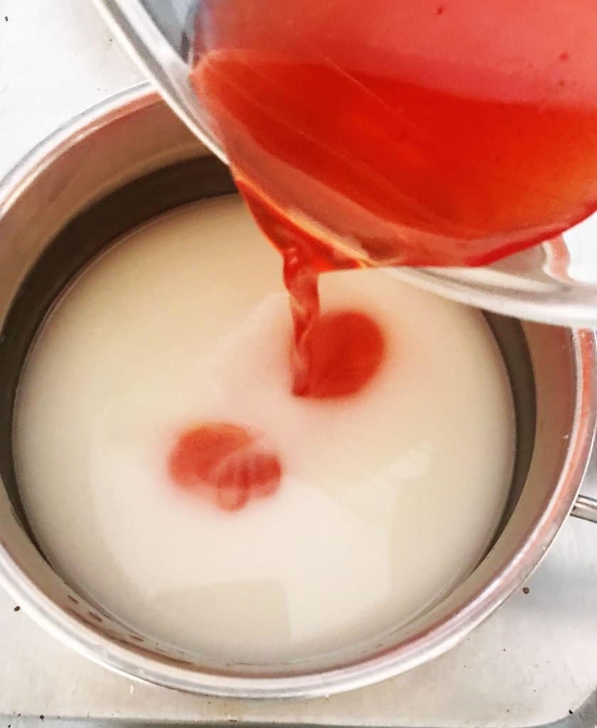 Saucepan with gelatin mixture and strawberry juice being poured in.