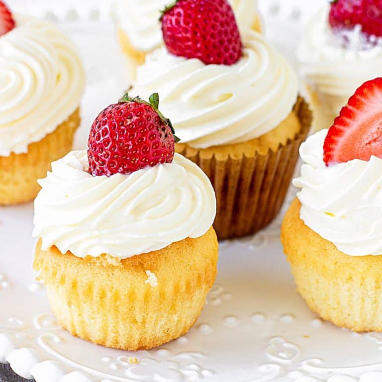 Several vanilla cupcakes topped with cream and fresh strawberries on white plate.