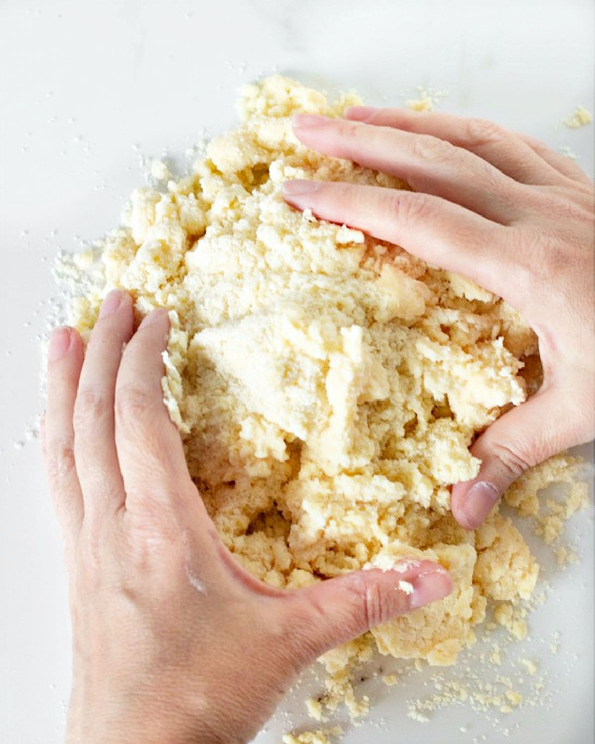 Hands gathering pie crust on a white marbled surface.