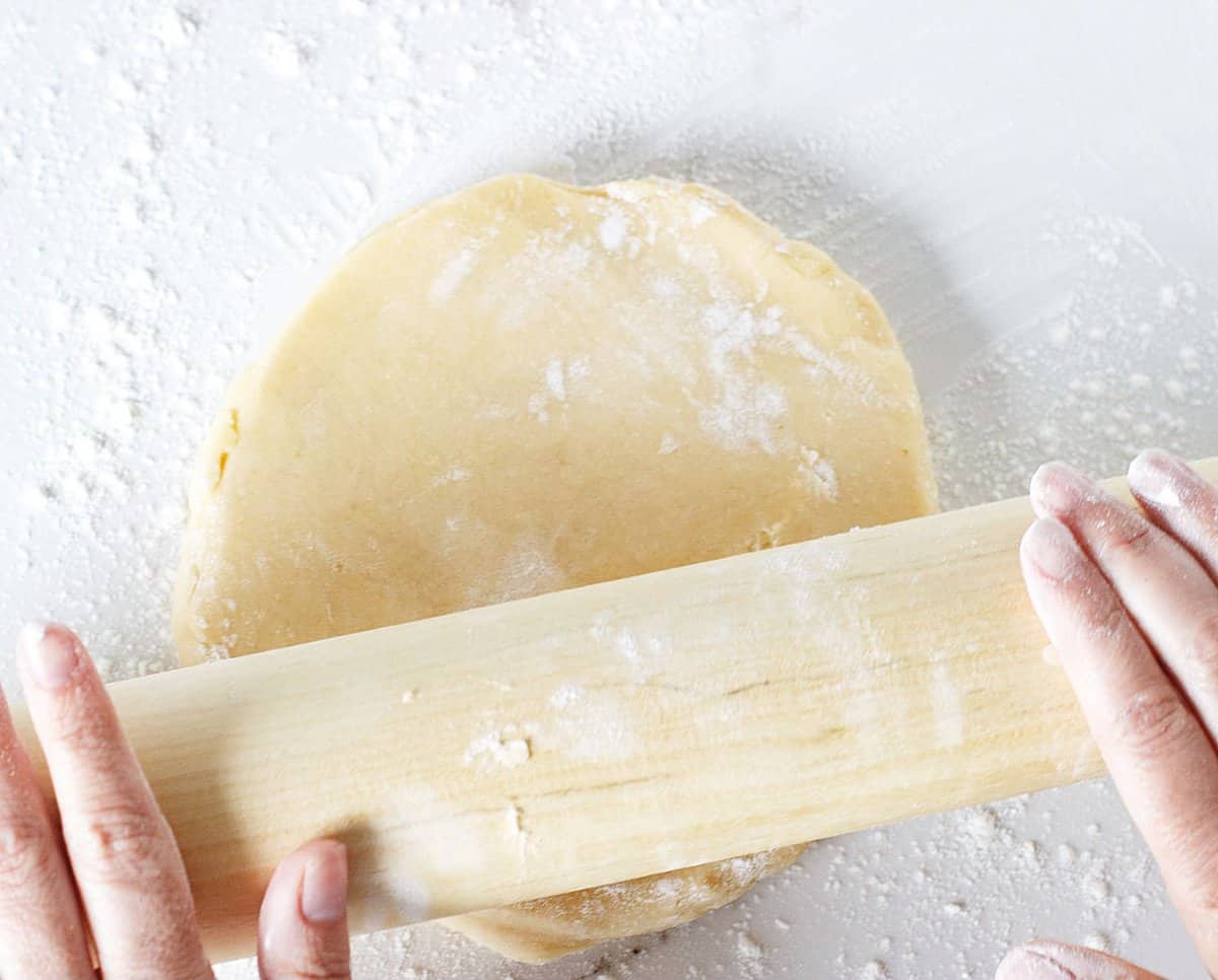 Rolling pie dough on white surface, light colored rolling pin.