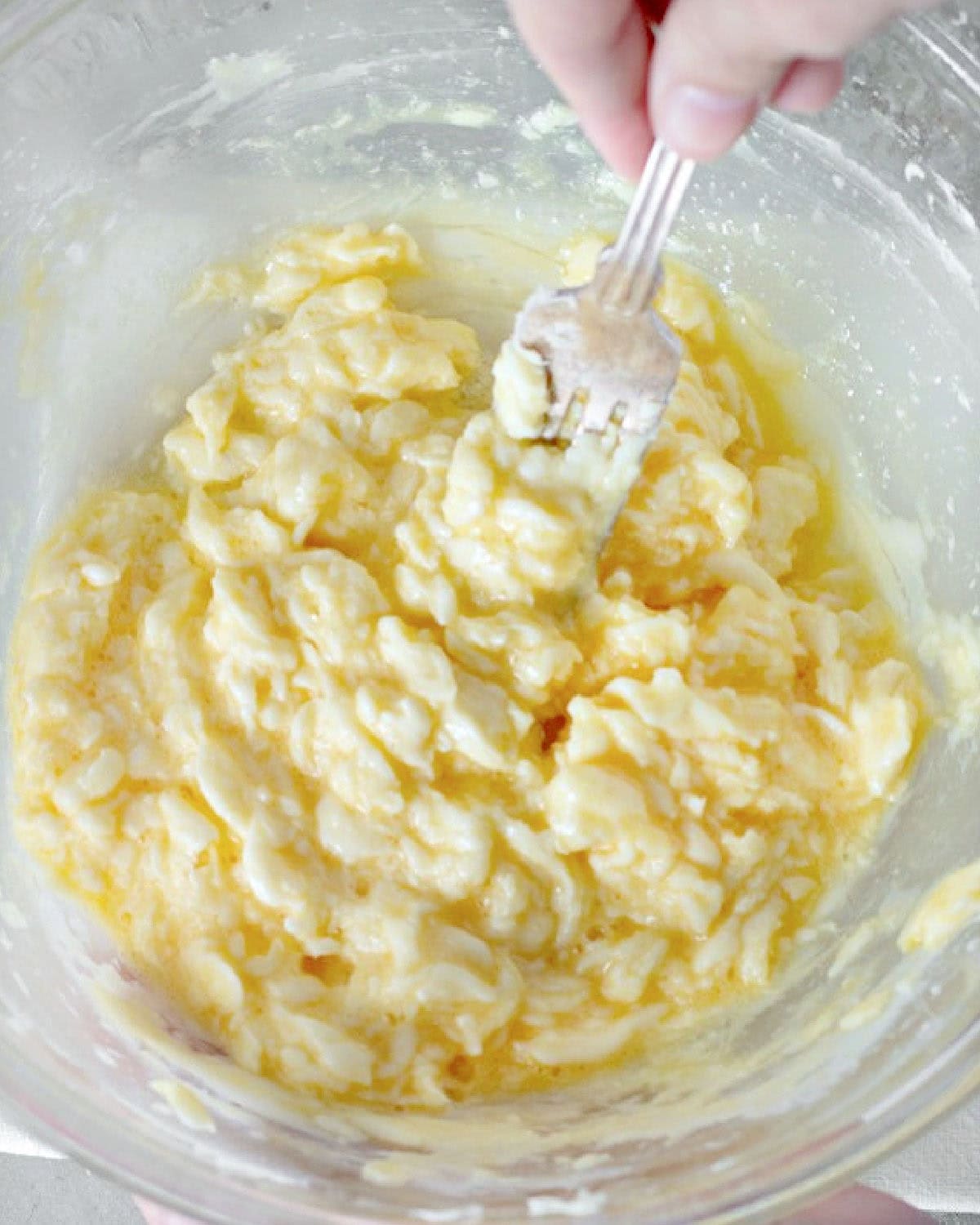 Stirring eggs and butter sugar mixture with a fork in a glass bowl.