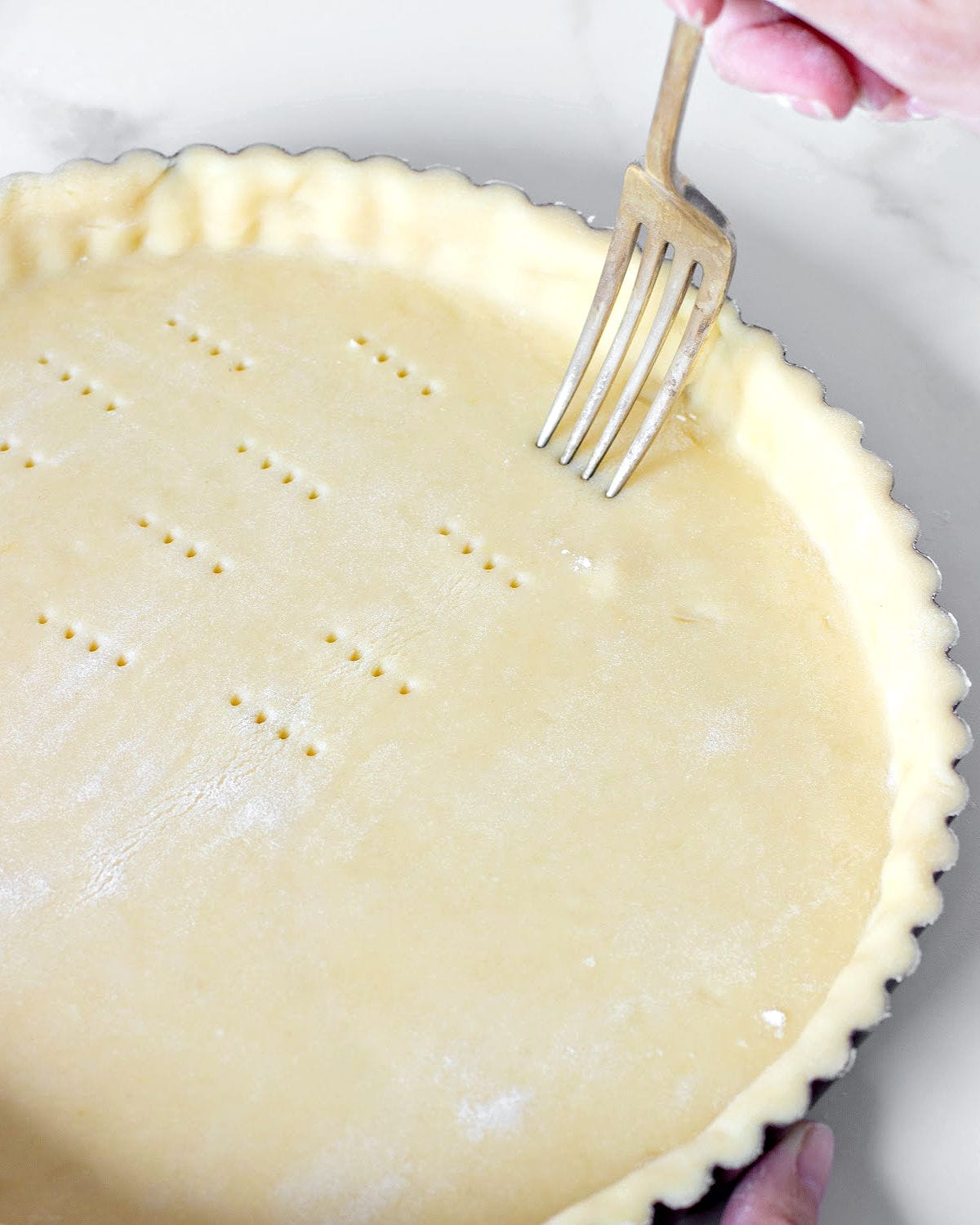 Pricking a tart crust with a fork on a white counter.