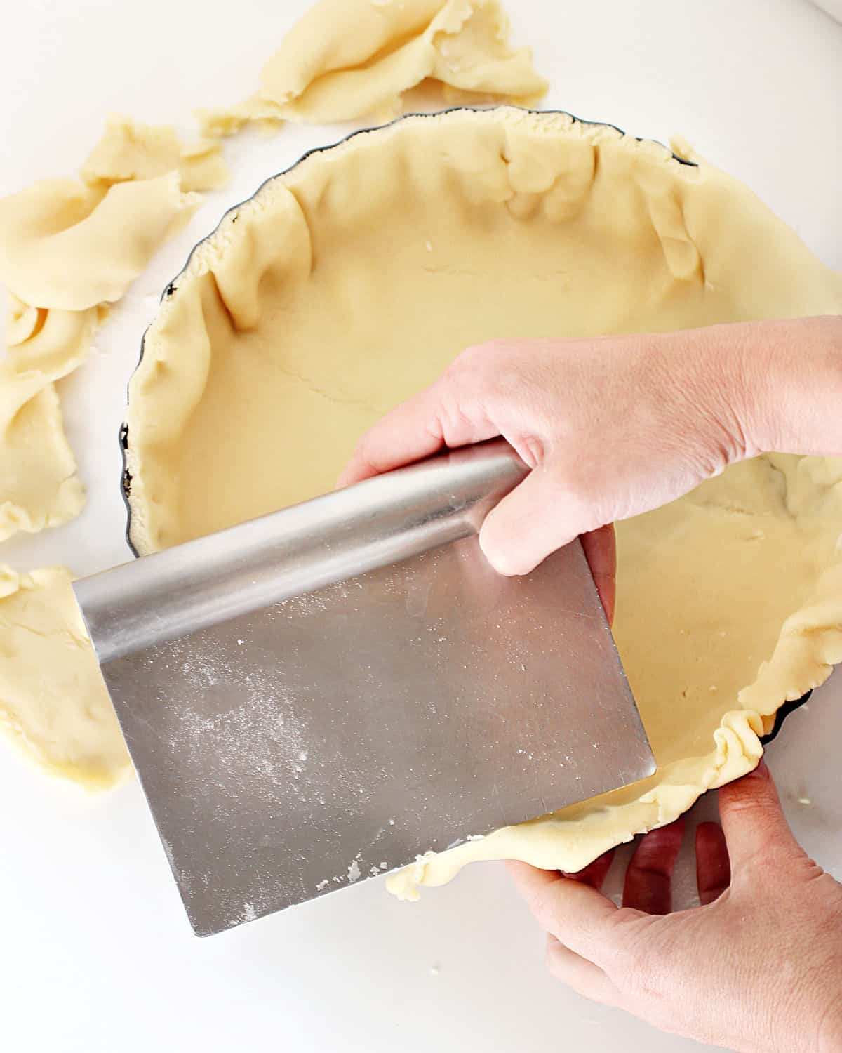 Removing excess dough with a dough scraper. Round pan, white background.
