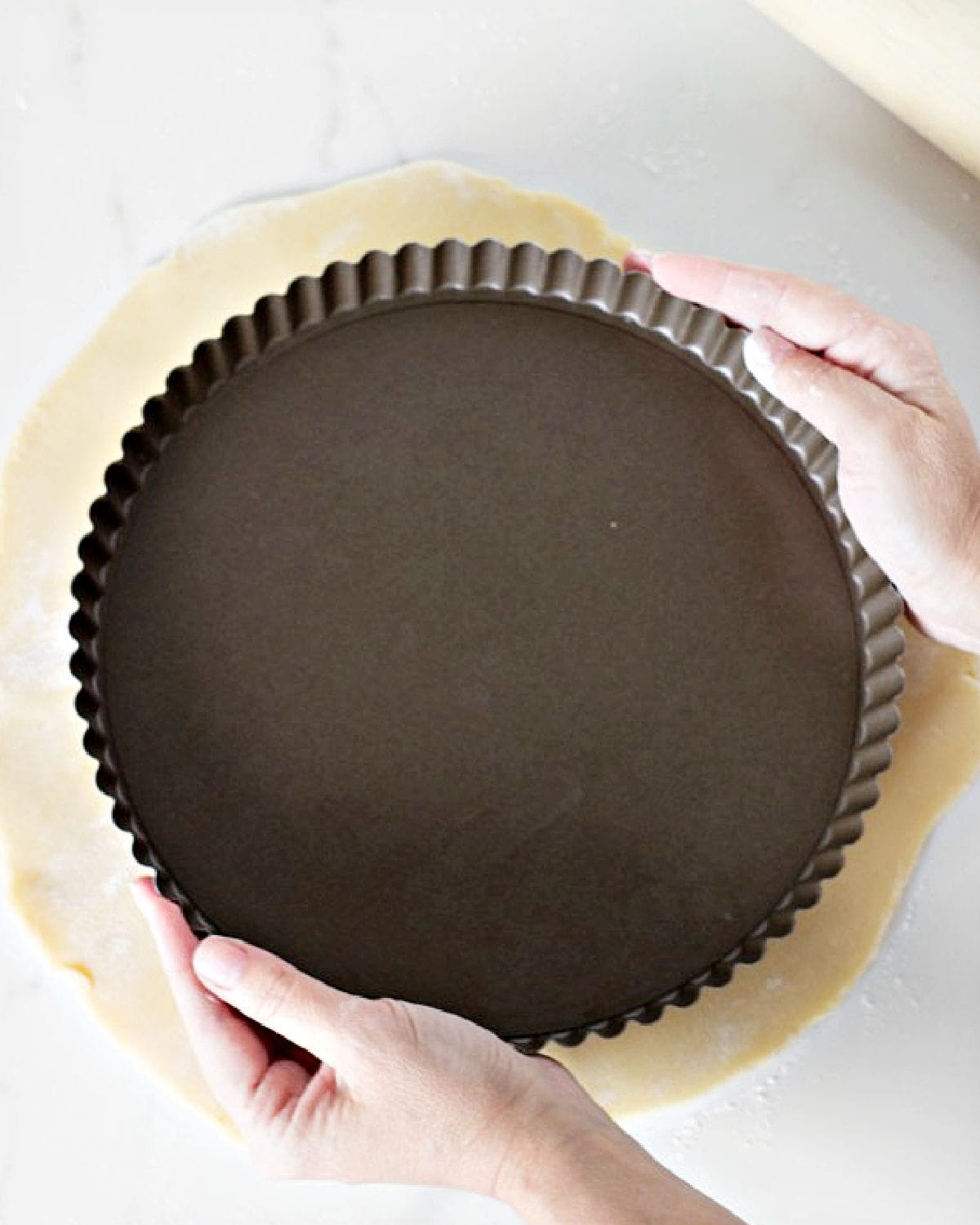 Measuring round dark pan over rolled pie crust. White marble surface.