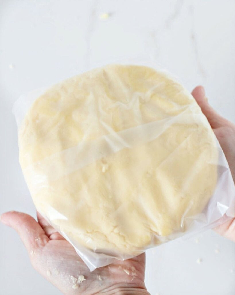 Wrapped dough disc being held. White marble background.