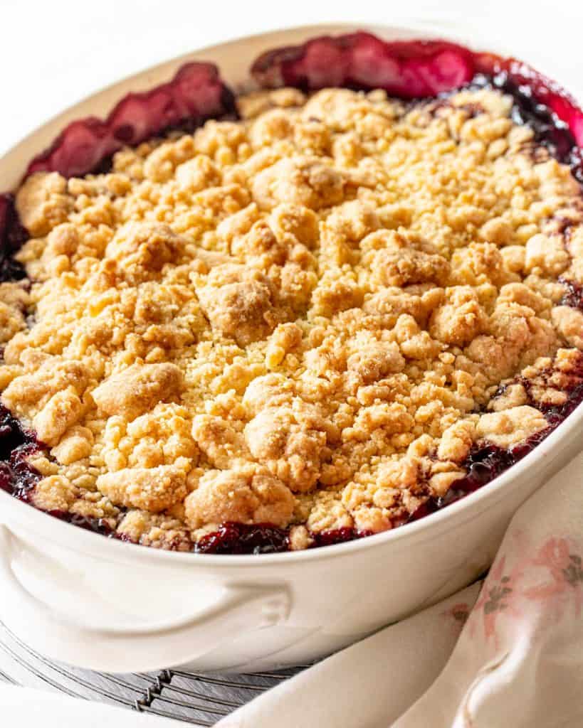 Baked cherry dump cake in oval white dish, white background, pink and white linen.
