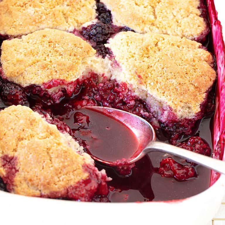 Silver spoon inside a baking dish with blackberry cobbler.