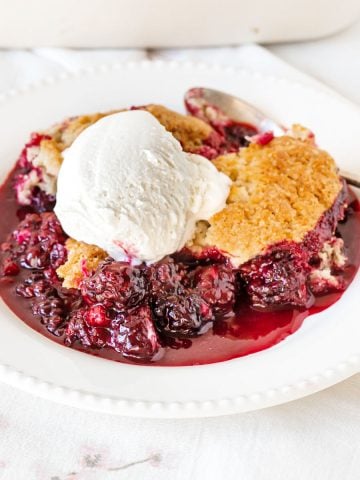 White plate with blackberry serving with ice cream on a white background.