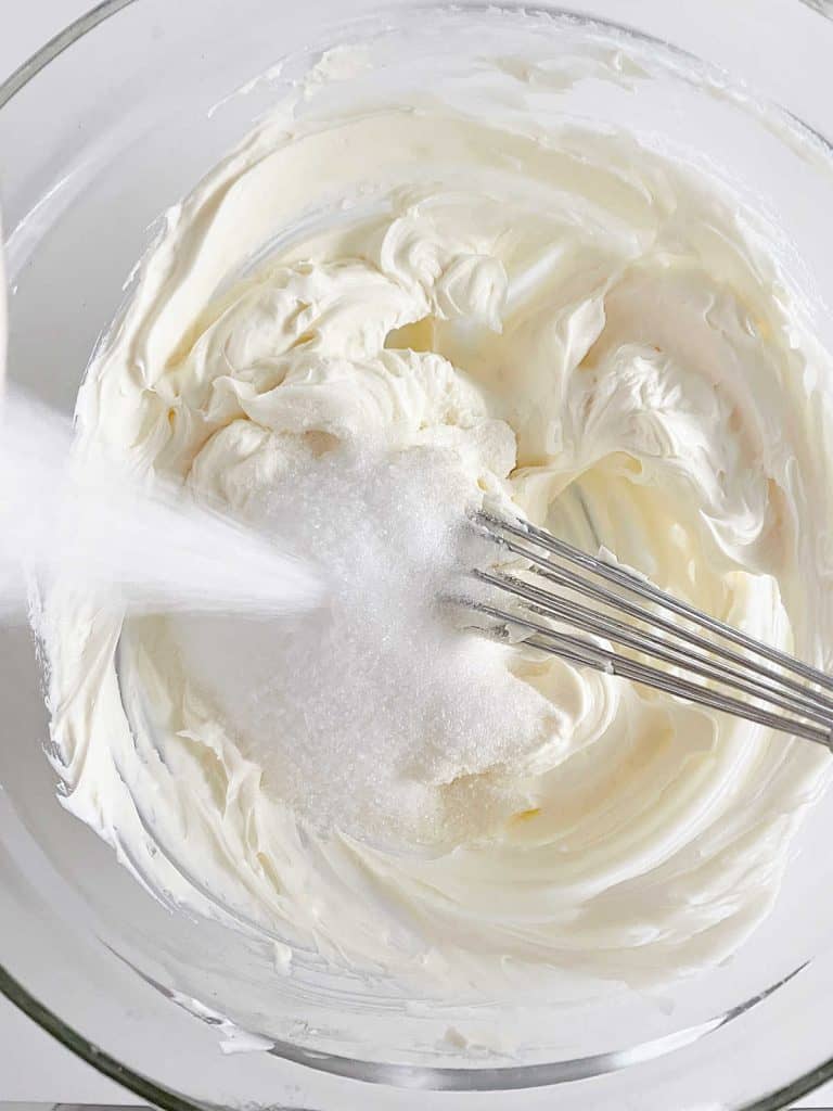 Mixing cream cheese and sugar in a glass bowl with a whisk.