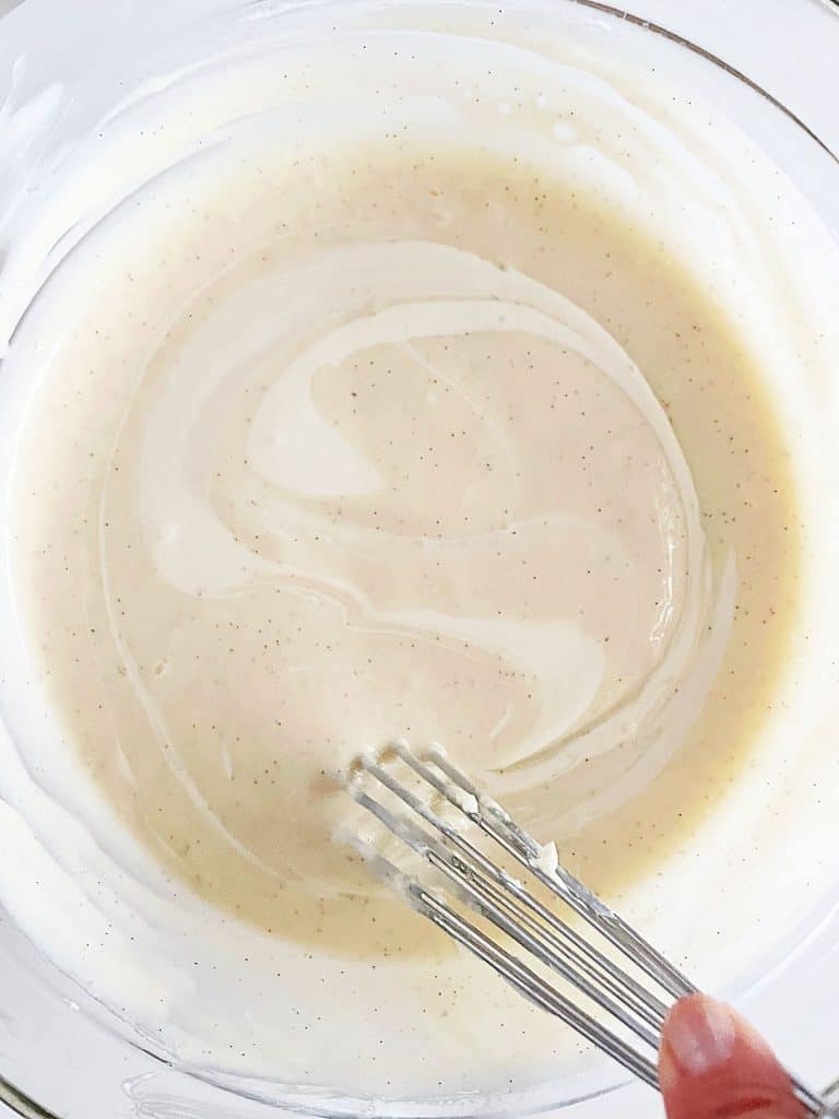 Stirring cheesecake batter in a glass bowl with a whisk.