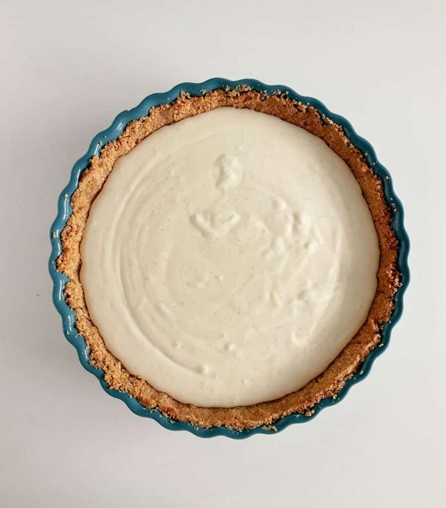 Teal round pie plate with cheesecake pie before baking. White background.