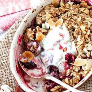 White individual dish with cherry crisp, silver spoon and melted ice cream, rustic background.