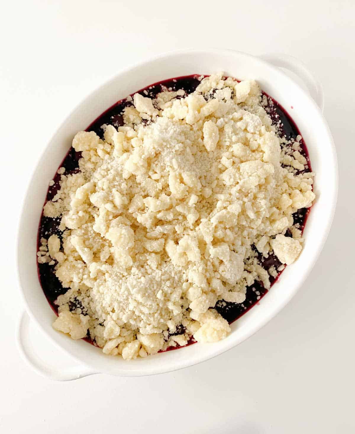Unbaked cherry dump cake in oval white dish on white surface, top view.