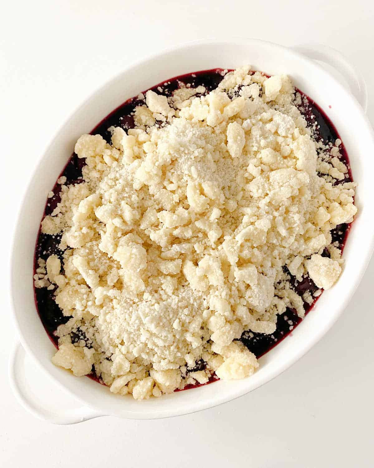 Unbaked cherry dump cake in oval white dish on white surface, top view.