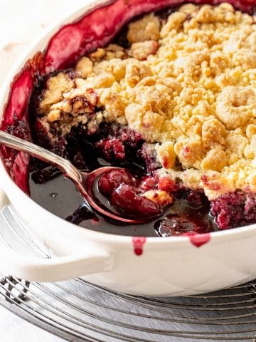 Close up of cherry cobbler in white oval dish on a wire rack.