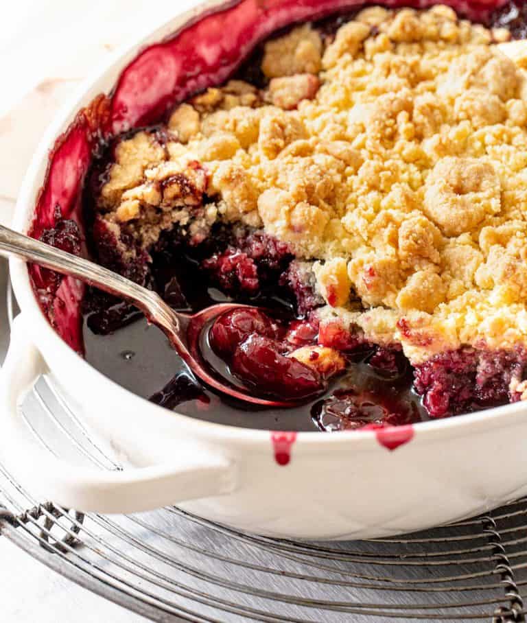 Close up of cherry cobbler in white oval dish on a wire rack.