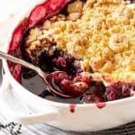Cherry dump cake on white oval dish on a wire rack with silver spoon inside.