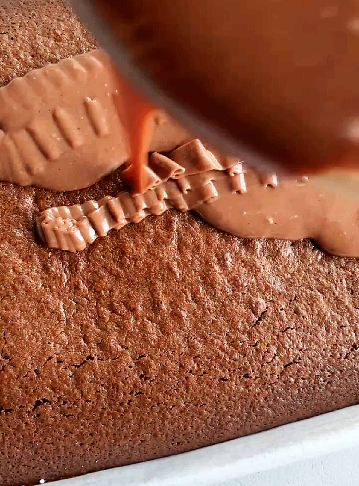 Pouring chocolate frosting on top of chocolate sheet cake.
